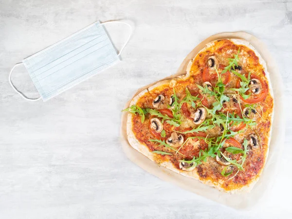 Herzförmige vegetarische Pizza mit medizinischer Maske auf grauem Tisch — Stockfoto