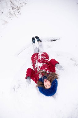 Kırmızı ceketli, karda yatan komik bir kadın.