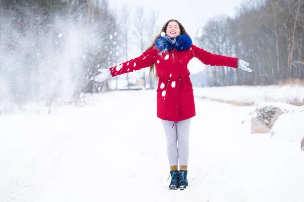 Ung kvinne i rød frakk som kaster snø – stockfoto