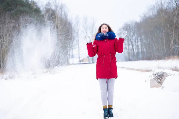 Ung kvinne i rød frakk som kaster snø – stockfoto