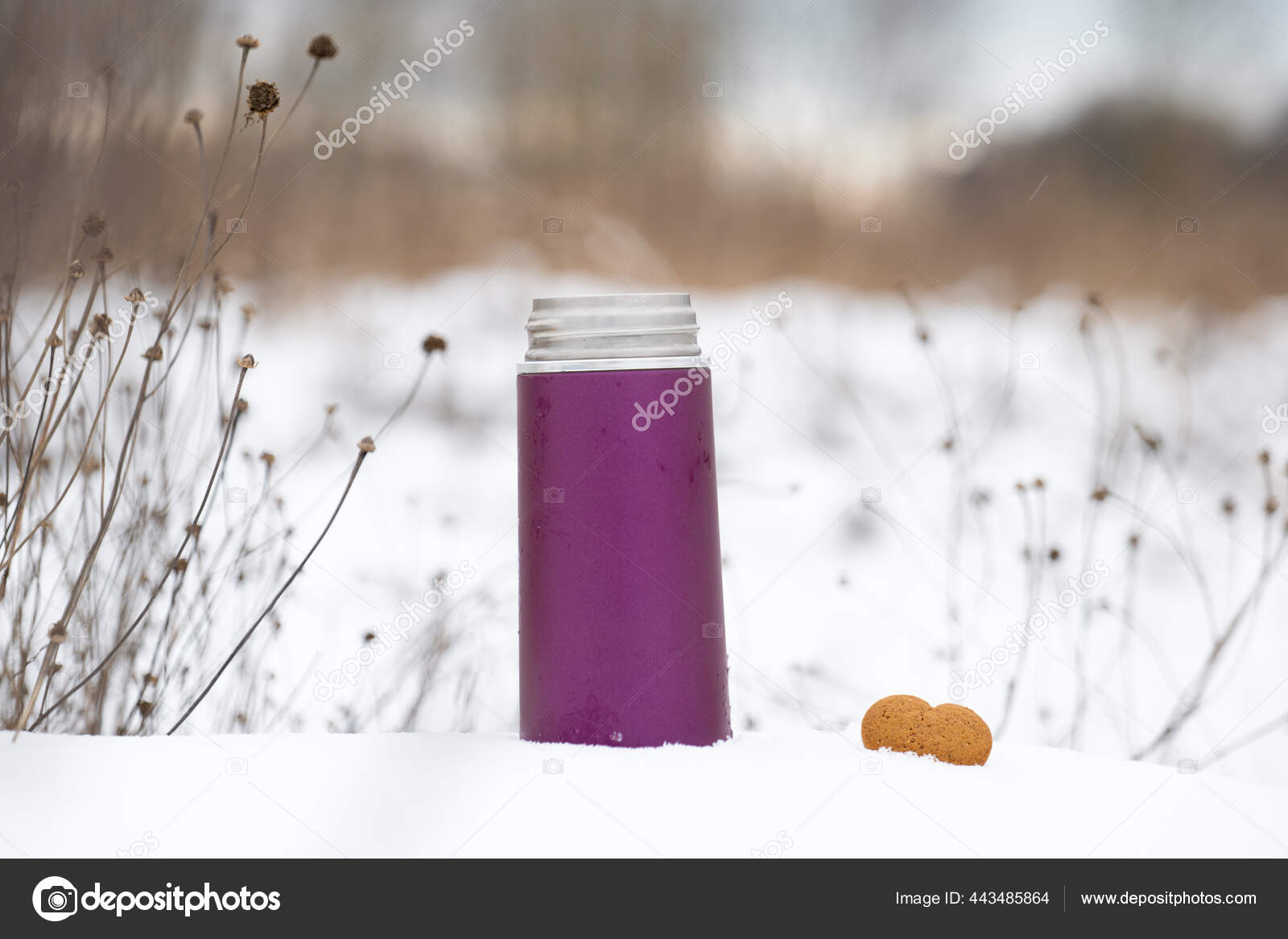 Small thermos with steaming hot drink on snow Stock Photo by