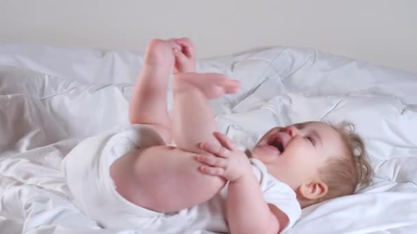 Imádnivaló 7 hónapos kislány fekszik az ágyon, és játszik a lábával — Stock videók