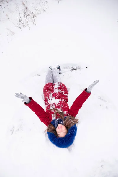 Jonge grappige vrouw in rode jas liggend op de sneeuw — Stockfoto