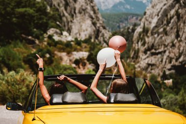 İki genç kadın ellerini kaldırıp tatilin tadını çıkarıyor.