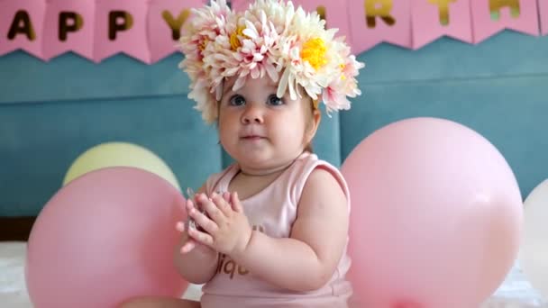 Adorable petite fille dans des fleurs couronne assis sur le lit avec des ballons sur son premier anniversaire — Video