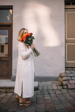 Bir kadın zarif bir şekilde kaldırım taşı sokağında yürüyor elinde canlı bir buket çiçekle..