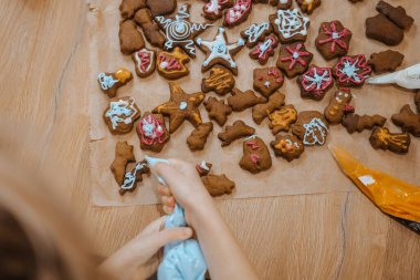 Bir insan, ahşap bir masanın üzerindeki renkli kremayla bir sürü kurabiyeyle kurabiye süslüyor..
