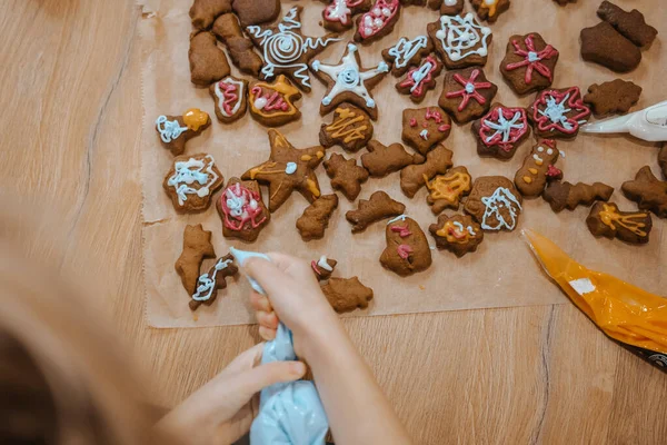 Bir insan, ahşap bir masanın üzerindeki renkli kremayla bir sürü kurabiyeyle kurabiye süslüyor..