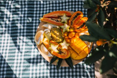 Taze kesilmiş tropikal meyveler güzel bir şekilde ahşap tabakta dizilmiş, gündüz bahçeyi aydınlatıyor..