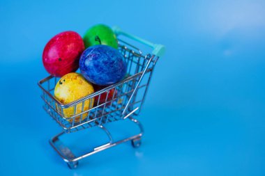 Paskalya yumurtaları mavi arka planda alışveriş arabasında mutlu paskalya konsepti. Paskalya indirimi.