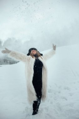 Soğuk bir kış gününde kadın derin bir karda durur ve neşeyle havaya kar atar..