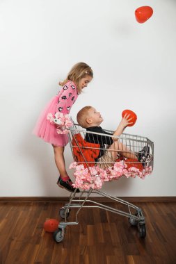 Bir kız alışveriş arabasında dururken, bir erkek elinde balonlarla oturuyor. Parlak bir mekanda vakit geçirmekten hoşlanırlar..