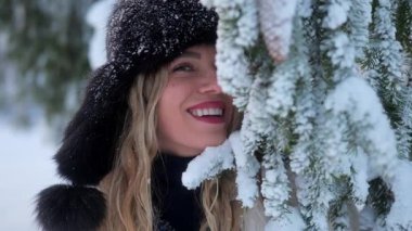Bir kadın kışın dışarıda durur, etrafı karla kaplı ağaçlar ve parlak bir atmosferle çevriliyken gülümser..