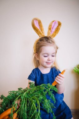 Paskalya günü tavşan kulağı takan şirin bir kız çocuğu. Komik. 3 yaşındaki kız elinde havuç tutuyor.