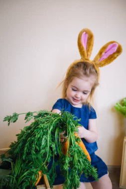 Paskalya günü tavşan kulağı takan şirin bir kız çocuğu. Komik. 3 yaşındaki kız elinde havuç tutuyor.