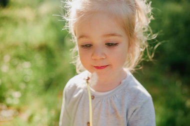 Bahar güneşli arka planında karahindiba ile gülümseyen 3 yaşındaki tatlı kız.
