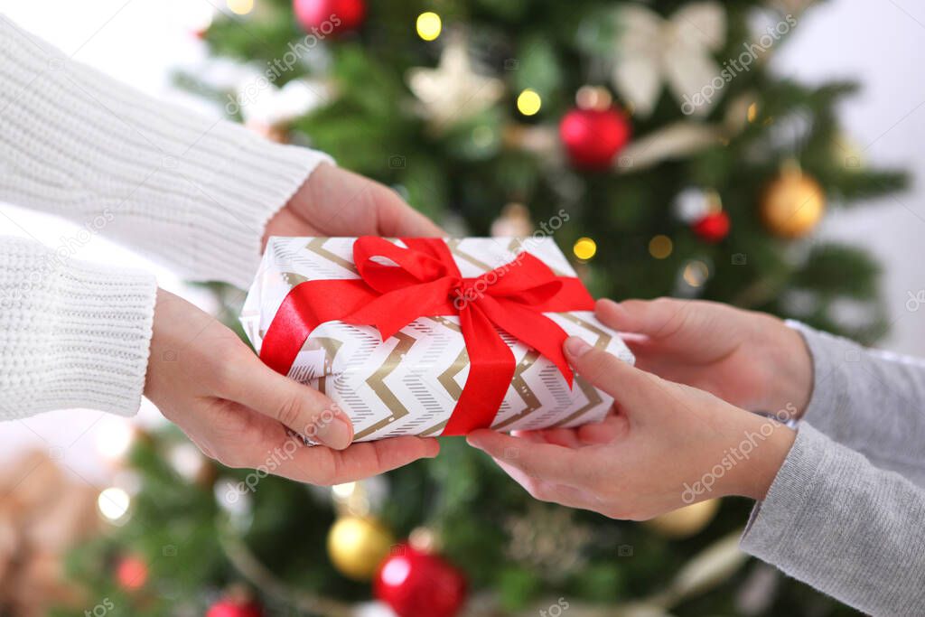 Christmas or New Years gift in hands against the background of a decorated interior. Give christmas gifts
