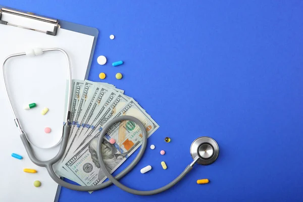 Medicinskt stetoskop och pengar på en färgad bakgrund ovanifrån närbild — Stockfoto
