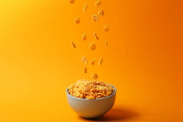 Delicious cornflakes falling into a plate on a colored background. — Stock Photo, Image