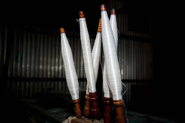 White yarn spools close-up in a yarn factory. White yarn spools in dark background.