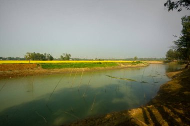 İnce kurumuş nehir kıyıları, sarı-yeşil mahsul toprakları ve mavi gökyüzü manzarası.