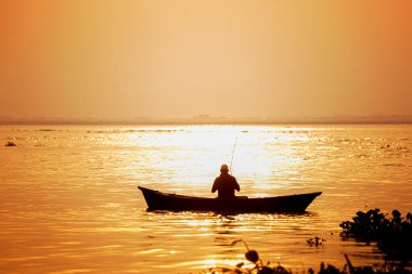 Akşam vakti, bir balıkçı teknede deniz kenarında balık tutuyor..