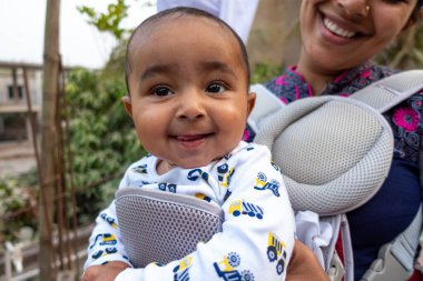 Bir anne, sevimli bebeğiyle taşınabilir bir çantanın içinde eğleniyor. Sevgi dolu sevgi dolu duygular. Aile ilişkisi ve anne-bebek bakımı kavramı.