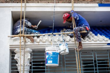 Joypara, Dohar, Dhaka, Bangladeş 'teki bir binanın beton duvarını tehlikeli ve riskli yollarla boyayan iki işçi. 18 Şubat 2021.