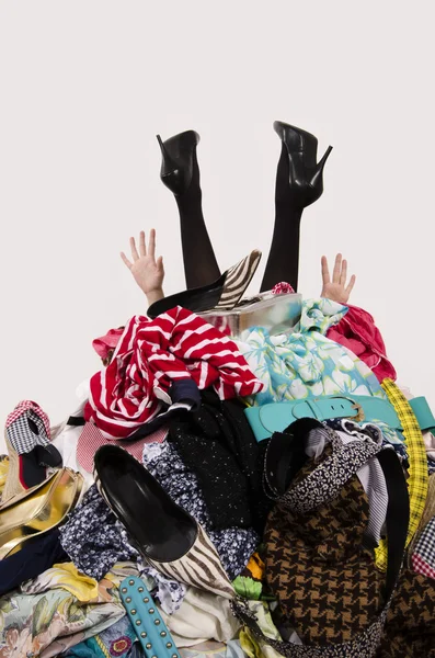 Vrouw benen en handen reiken van een grote stapel van kleding en accessoires. — Stockfoto