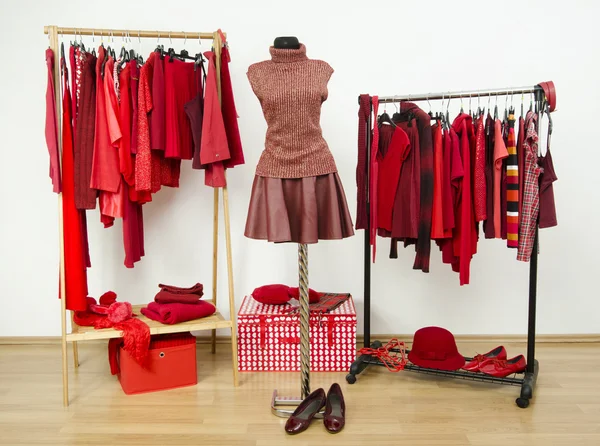 Armario con ropa roja dispuesta en perchas y un traje en un maniquí . — Foto de Stock