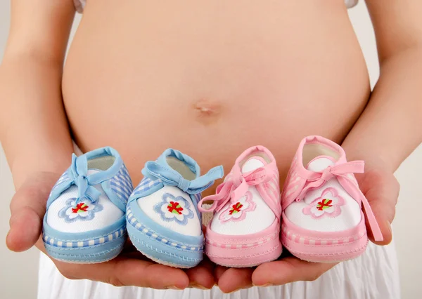 De cerca en el vientre embarazada con zapatos recién nacidos de color rosa y azul . — Foto de Stock