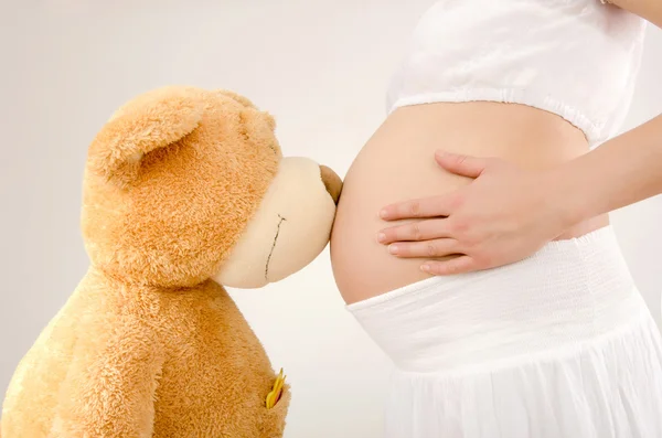 Close up on pregnant belly and a big teddy bear. — Stock Photo, Image