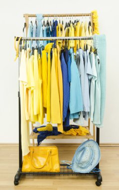 Wardrobe with shades of yellow and blue clothes hanging on a rack nicely arranged. clipart