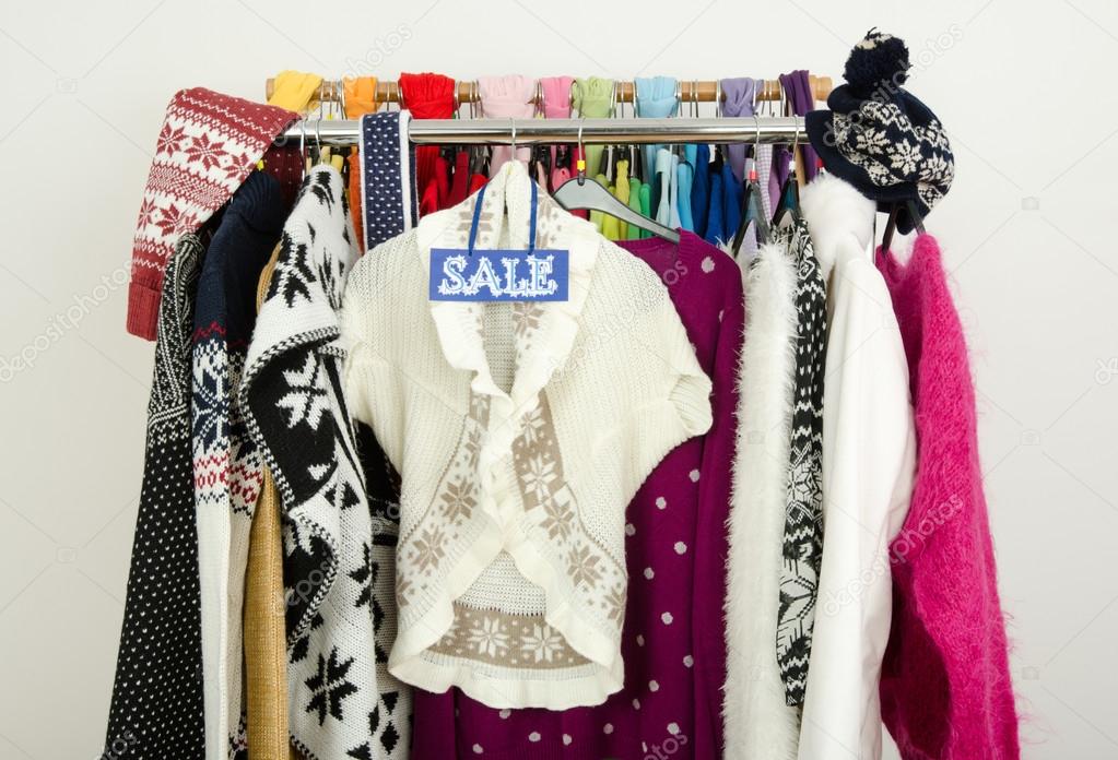 Cute winter sweaters displayed on hangers with a big sale sign.