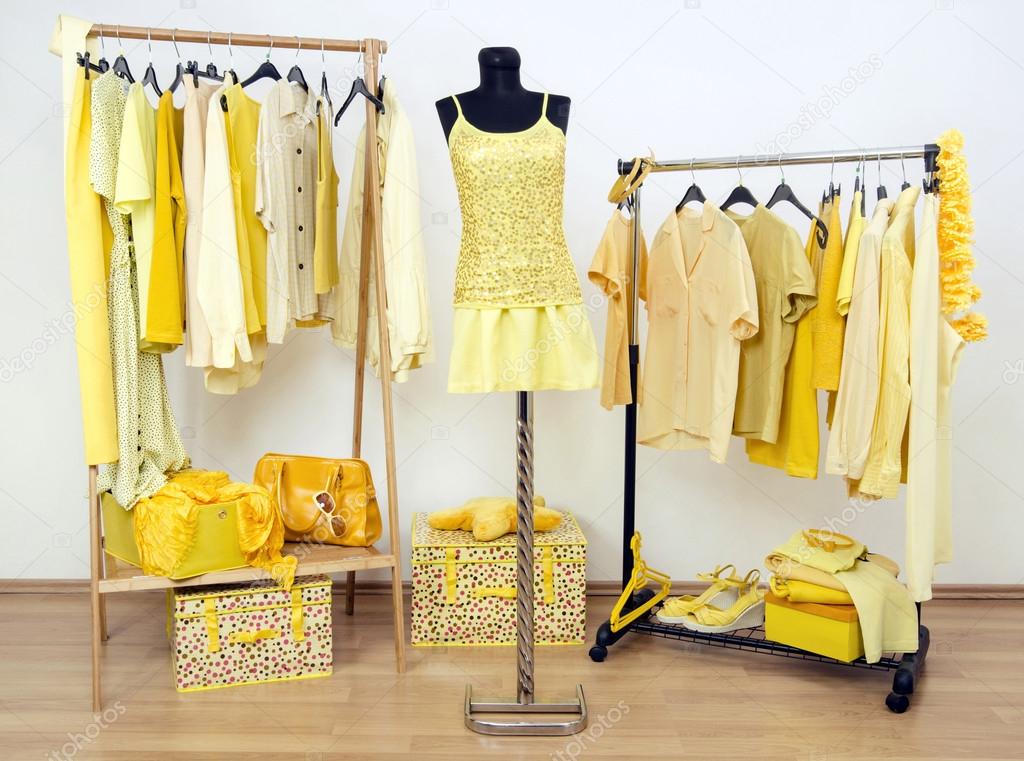 Dressing closet with yellow clothes arranged on hangers and an outfit on a mannequin.