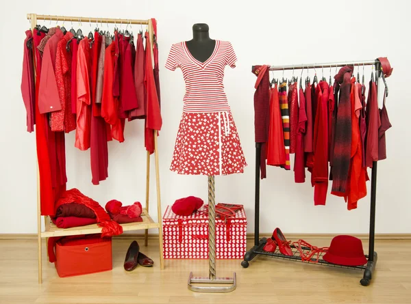 Dressing closet with red clothes arranged on hangers and an outfit on a mannequin.