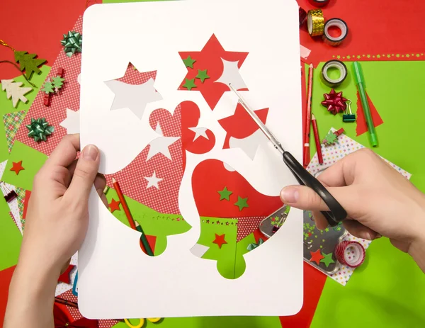 Χέρι μιας γυναίκας κοπή ένα λευκό χαρτόνι με Χριστουγεννιάτικα σχήματα., αστέρια και κουδούνια. — Φωτογραφία Αρχείου