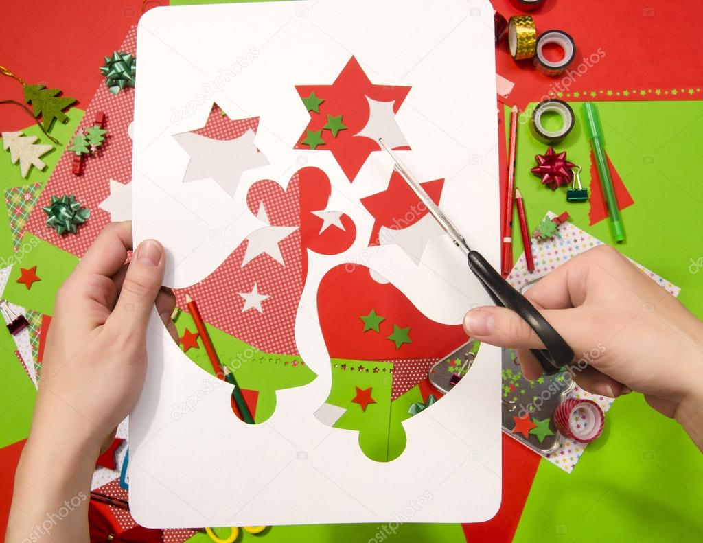 Hand of a woman cutting a white cardboard  with Christmas shapes., stars and bells.