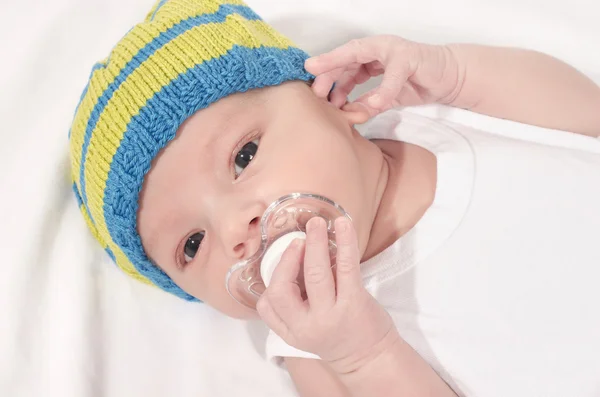 Bayi cantik berbaring di atas lembaran putih dengan dot di mulutnya . — Stok Foto