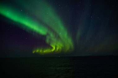 Kuzey Işıkları 'nın nefes kesen manzarası okyanus üzerindeki gece gökyüzünü aydınlatır ve büyüleyici yeşil ve mor renkler yaratır.