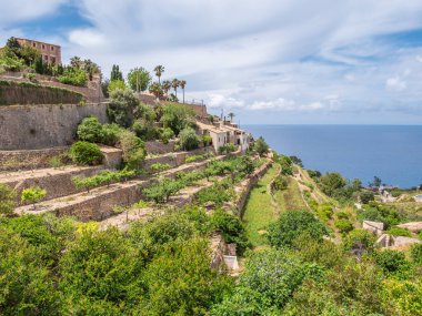 Banyalbufar, Mallorca. Teraslı bahçeleri ve tarihi binaları olan pitoresk kıyı köyü bir yamaçta, parçalı bulutlu gökyüzünün altında, denize bakan Mayorka 'da bulunur.