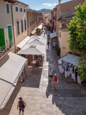 Alcudia pazarı, Mallorca, alışveriş merkezleri ve açık kafelerle dolu, güneşli bir günde gezen ve eğlenen insanlarla dolu, ilginç bir kasabada hareketli bir cadde.