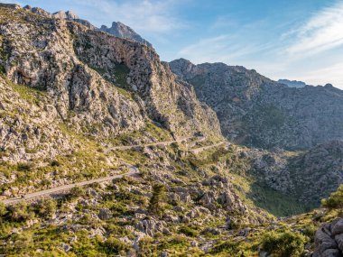 Sa Calobra, Mallorca 'ya giden Serpentine yolu, engebeli, yeşil bitki örtüsü ile kayalık arazide kıvrılan dağ yolu yılanları, açık mavi gökyüzünün altında yükselen tepeler zeminine kurulur, Majorca.