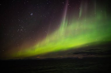 Kuzey Işıkları 'nın nefes kesen manzarası Aurora Borealis gece gökyüzünü engin ve karanlık bir manzaranın üzerinde aydınlatır.