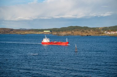 Norveç 'te küçük bir köyü olan, dağlık bir sahil şeridinde, sakin sularda ilerleyen kırmızı bir gemi var.