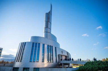 Kuzey Işıkları Katedrali, Alta, Norveç, modern kilise kendine özgü bir kulesi ve kıvrımlı mimarisi olan açık mavi bir gökyüzünün altında, insanlar bir köprüde yürüyor.