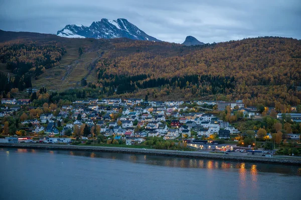 Narvik, Norveç. Sonbahar yapraklarıyla çevrili karlı dağların eteklerinde yuva yapmış pitoresk kasaba, akşam parıltısıyla aydınlanıyor.
