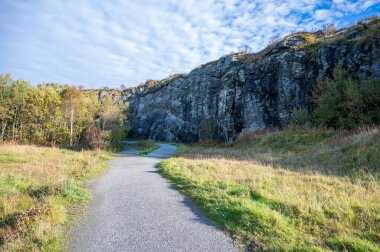 Kyststien, Haugesund, Norveç, Çimenli bir tarladan esen çakıl yolu parçalı bulutlu bir gökyüzünün altındaki kayalık bir uçuruma çıkıyor.