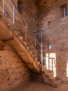 Alcudia, Mallorca, taş metal merdiven antik taş duvarlardan yükselir, bir pencereden süzülen güneş ışığıyla aydınlatılır, Mayorka