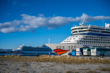 AIDA Bella adında büyük bir yolcu gemisi Norveç 'in Alta Limanı' na yanaştı. Zümrüt Prenses yolcu gemisi arka planda berrak mavi gökyüzünün altında görünüyor. Yakınlarda birkaç otobüs var.